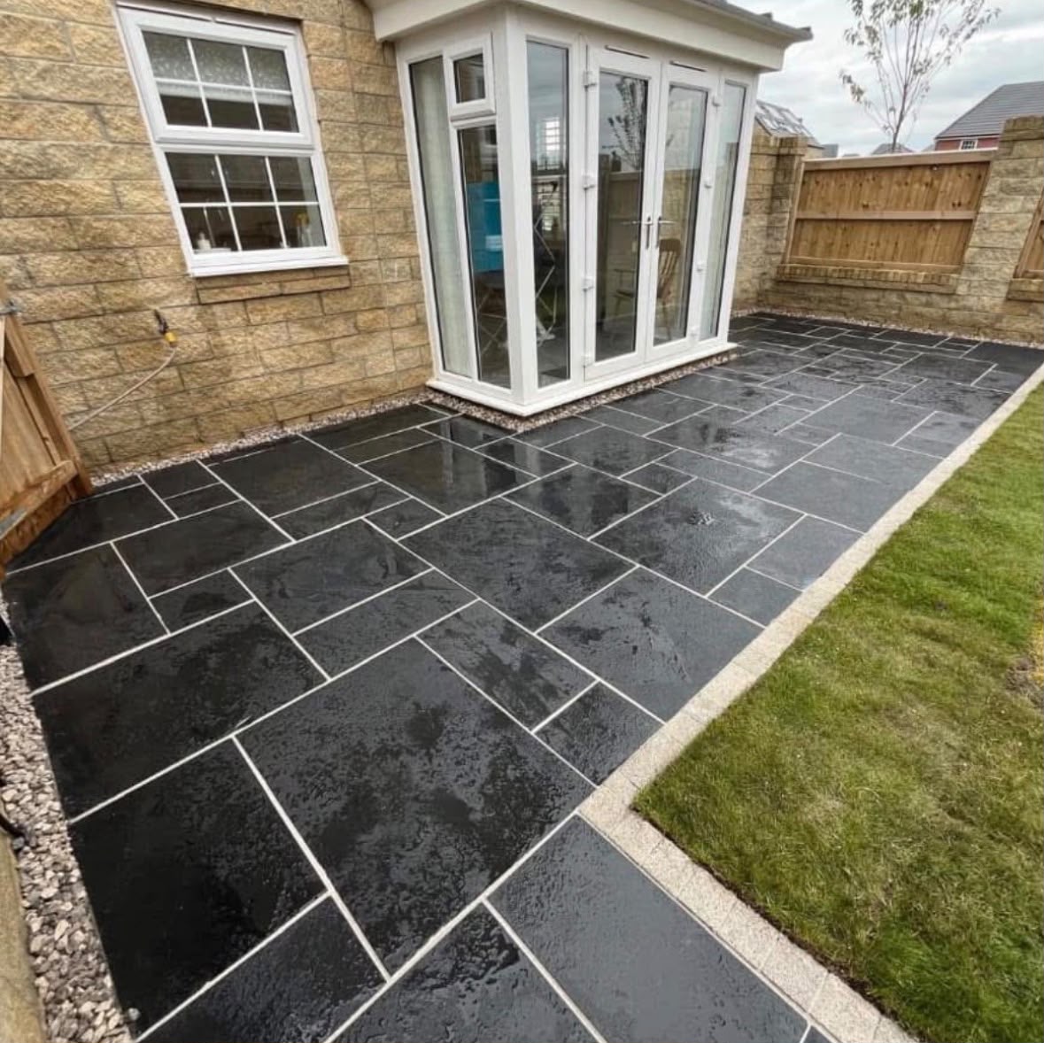 Black Indian stone patio with white pointing beside a lawn and conservatory