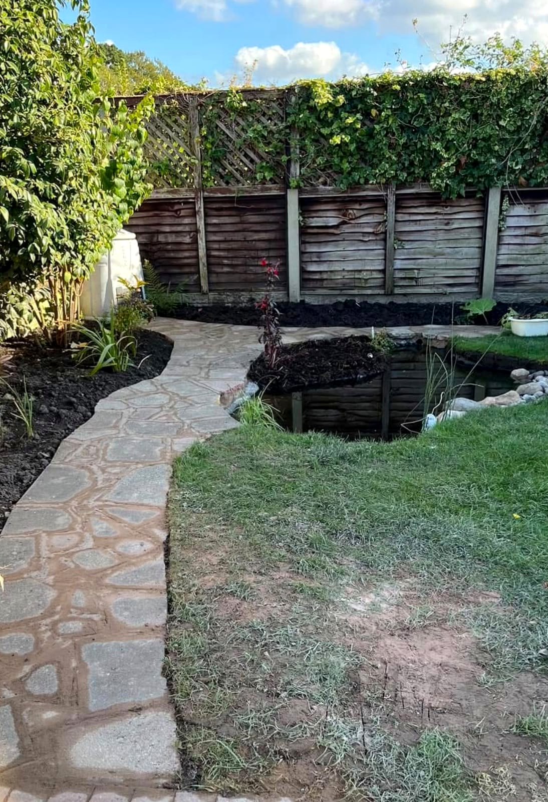 Garden pond with stone path, lawn and timber fence