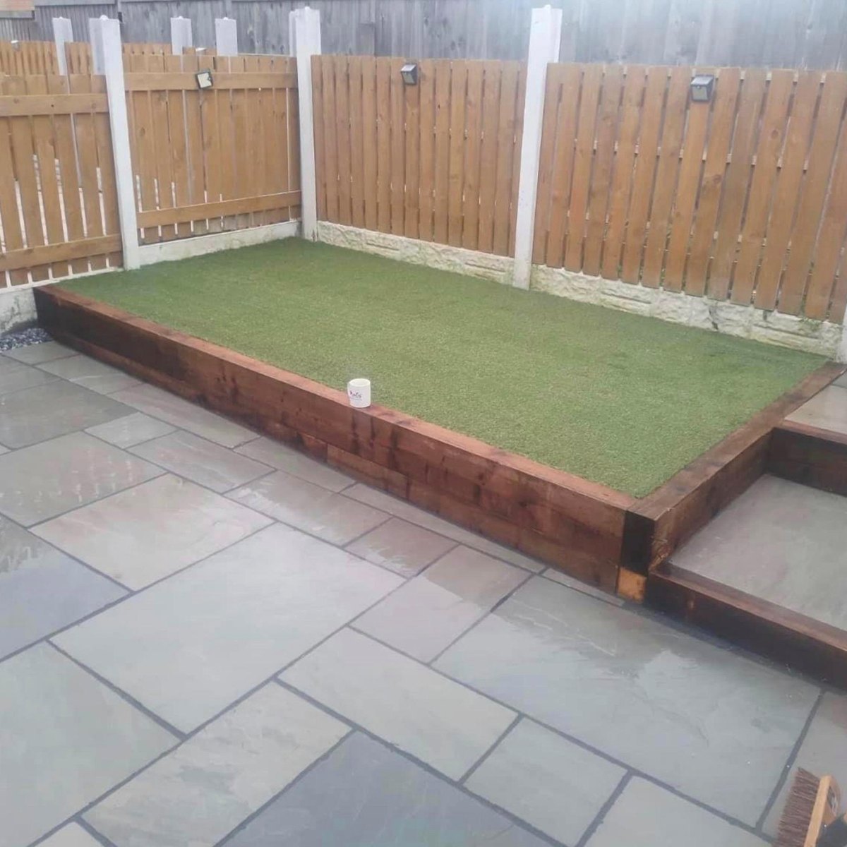 Raised sleeper lawn beside a flagged patio and fence
