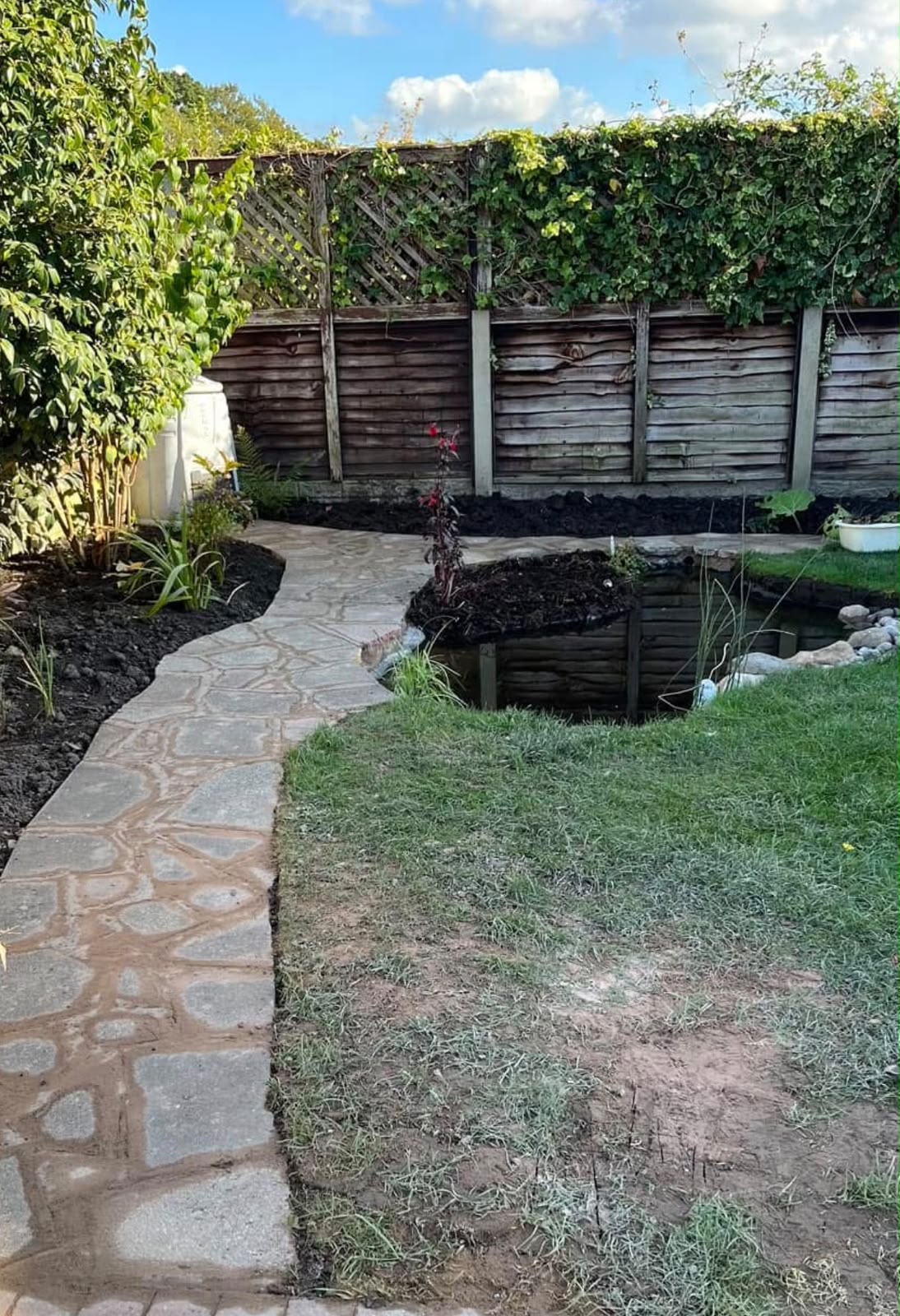 Garden pond with stone path, planting and a timber fence